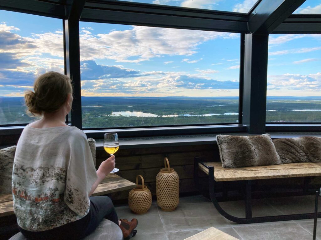 Nainen istuu Gold Digger Sky Loungessa, juo viinia ja nauttii tunturimaisemimsta.